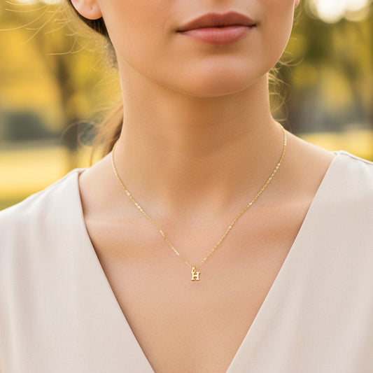 Cuello de modelo usando una cadena con un dije de la letra H mini en oro amarillo de 18 quilates de Joyería Caracas.