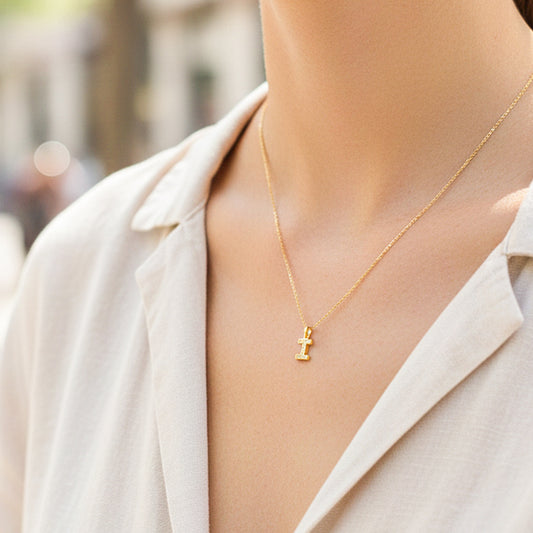 Cuello de modelo usando una cadena con un dije en forma de la letra I en oro amarillo de 18 quilates con cristales de Joyería Caracas.