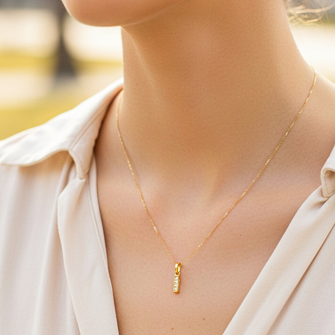 Cuello de modelo usando una cadena con un dije en forma de la letra I en oro amarillo de 18 quilates con cristales de Joyería Caracas.