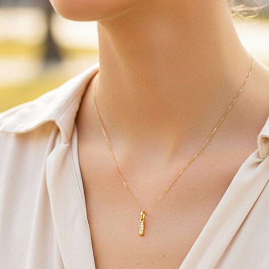 Cuello de modelo usando una cadena con un dije en forma de la letra I en oro amarillo de 18 quilates con cristales de Joyería Caracas.