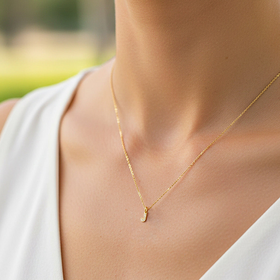 Cuello de modelo usando una cadena con un dije en forma de letra J mini en oro amarillo de 18 quilates con cristales de Joyería Caracas.