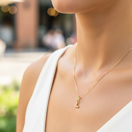 Cuello de modelo usando una cadena con un dije en forma de la letra L en oro amarillo de 18 quilates con cristales de Joyería Caracas.