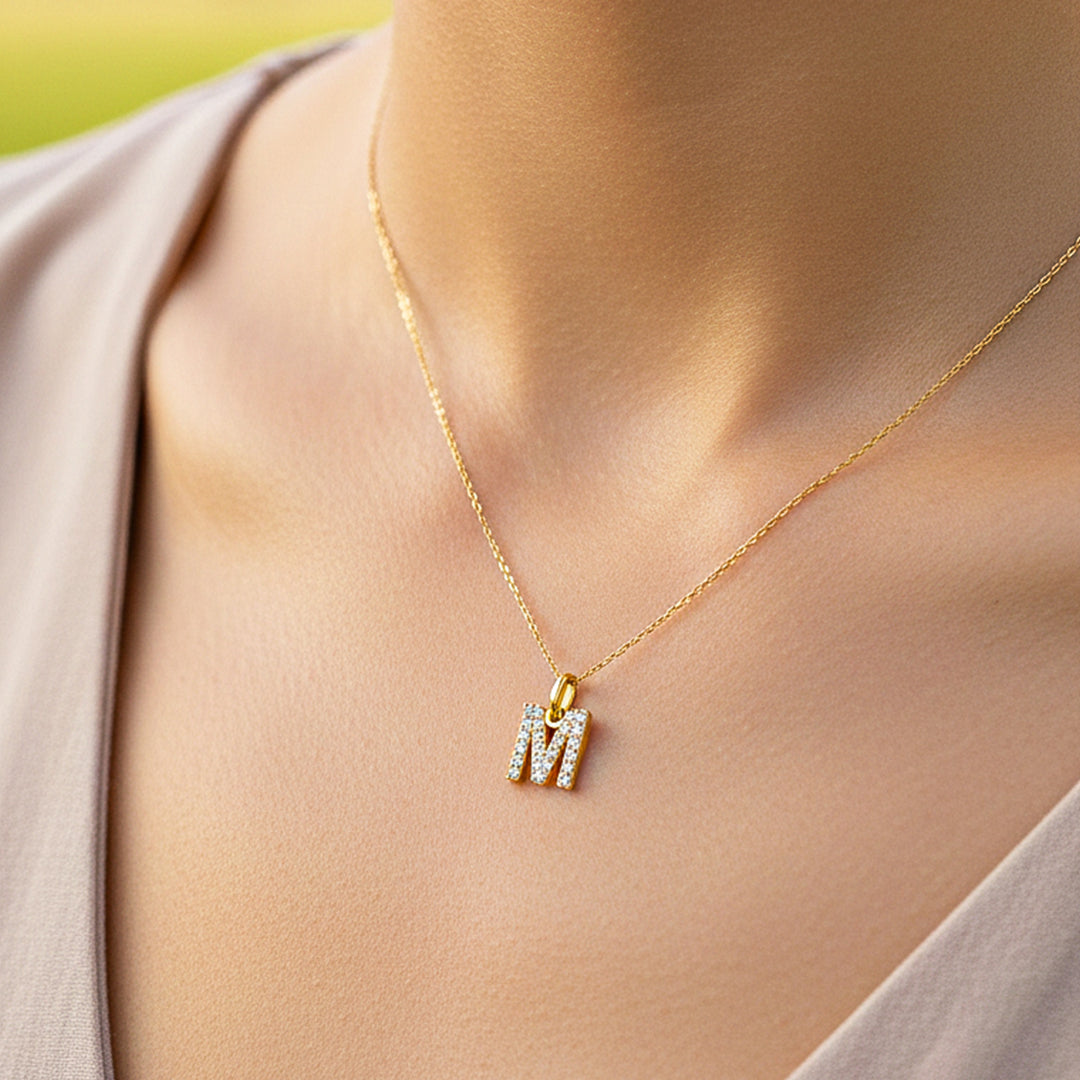 Cuello de modelo usando una cadena con un dije en forma de la letra M en oro amarillo de 18 quilates con cristales de Joyería Caracas.