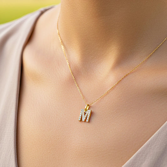 Cuello de modelo usando una cadena con un dije en forma de la letra M en oro amarillo de 18 quilates con cristales de Joyería Caracas.