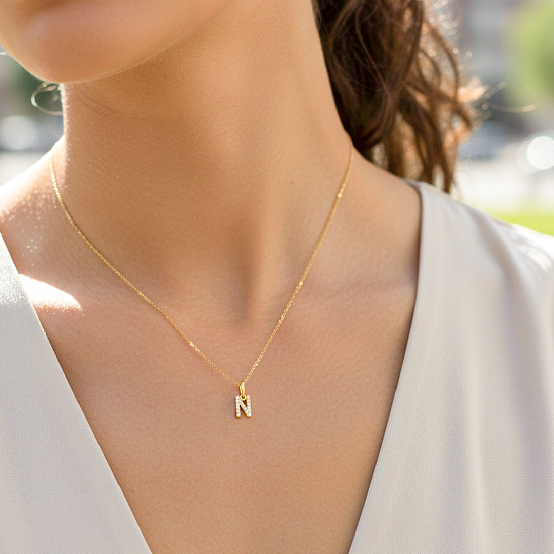 Cuello de modelo usando una cadena con un dije de la letra N en oro amarillo de 18 quilates con cristales de Joyería Caracas.