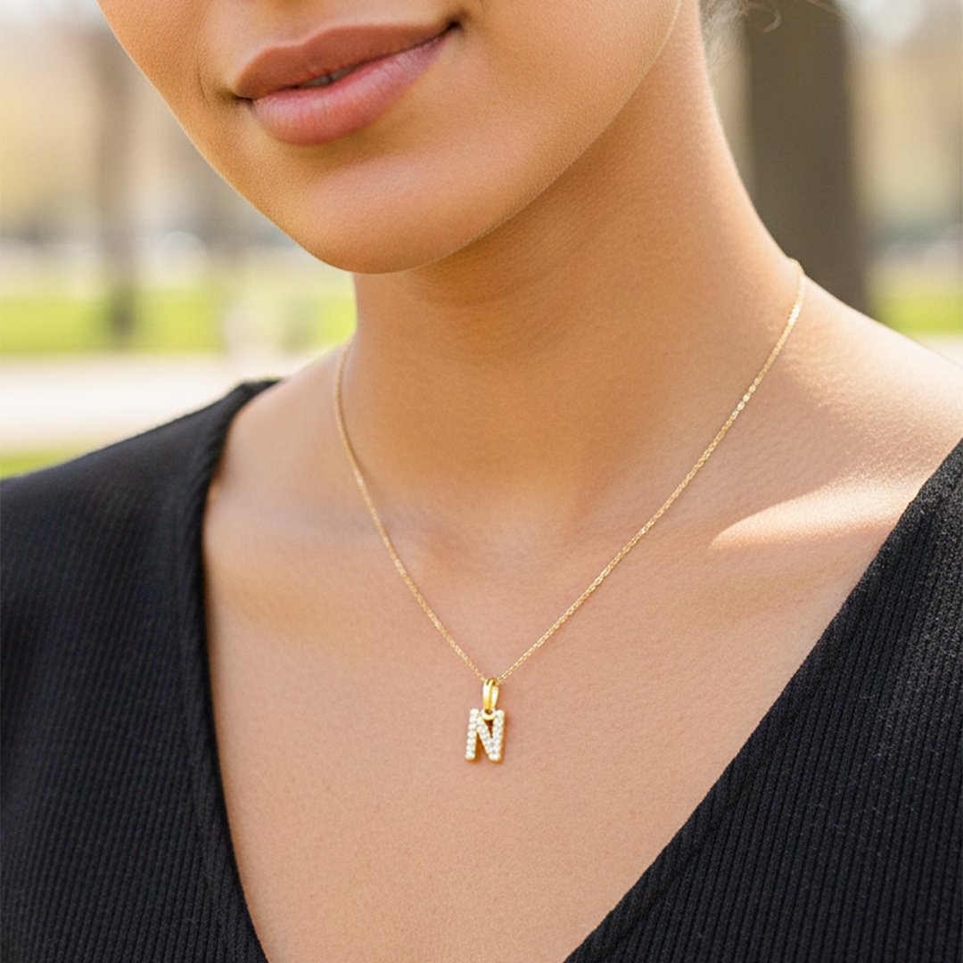 Cuello de modelo usando una cadena con un dije en forma de la letra N en oro amarillo de 18 quilates con cristales de Joyería Caracas.