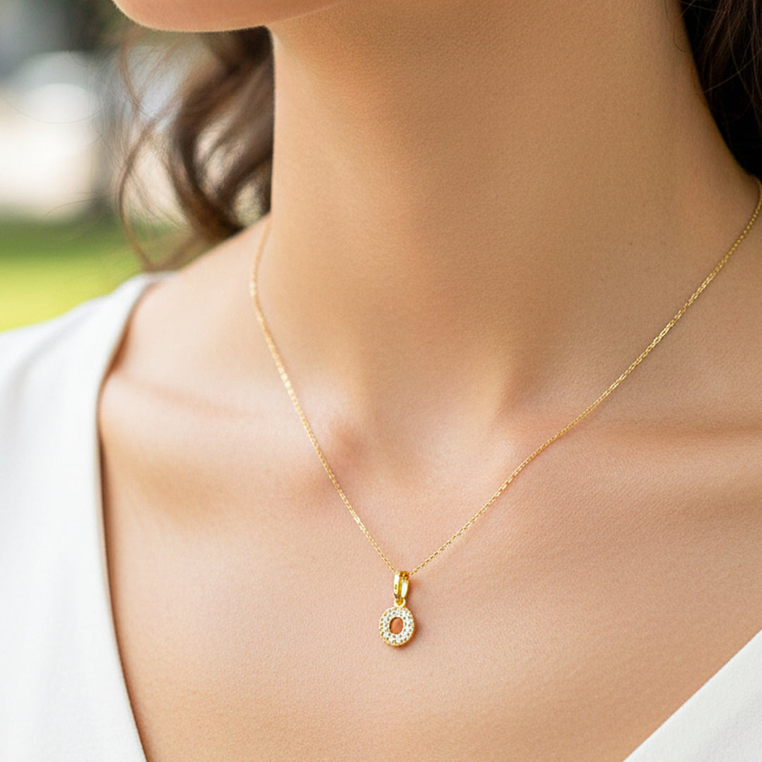 Cuello de modelo usando una cadena con un dije en forma de la letra O en oro amarillo de 18 quilates con cristales de Joyería Caracas.