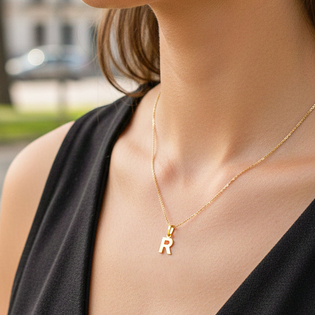 Cuello de modelo usando una cadena con un dije en forma de letra R en oro amarillo de 18 quilates de Joyería Caracas.