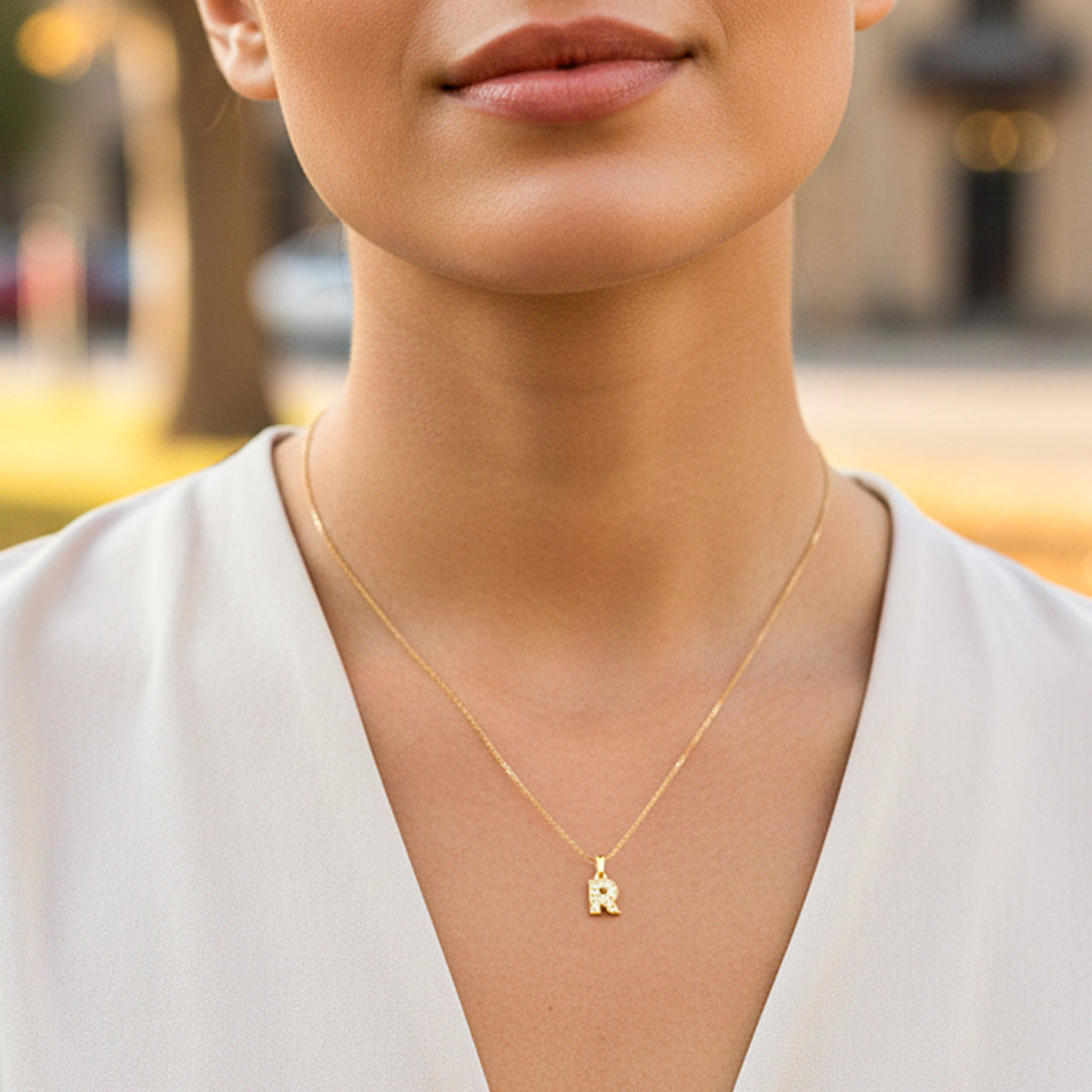 Cuello de modelo usando una cadena con un dije en forma de la letra R en oro amarillo de 18 quilates con cristales de Joyería Caracas.