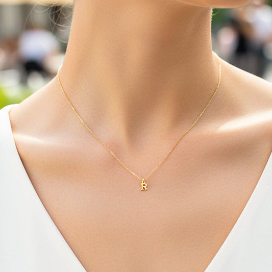 Cuello de modelo usando una cadena con un dije en forma de letra R en oro amarillo de 18 quilates de Joyería Caracas.