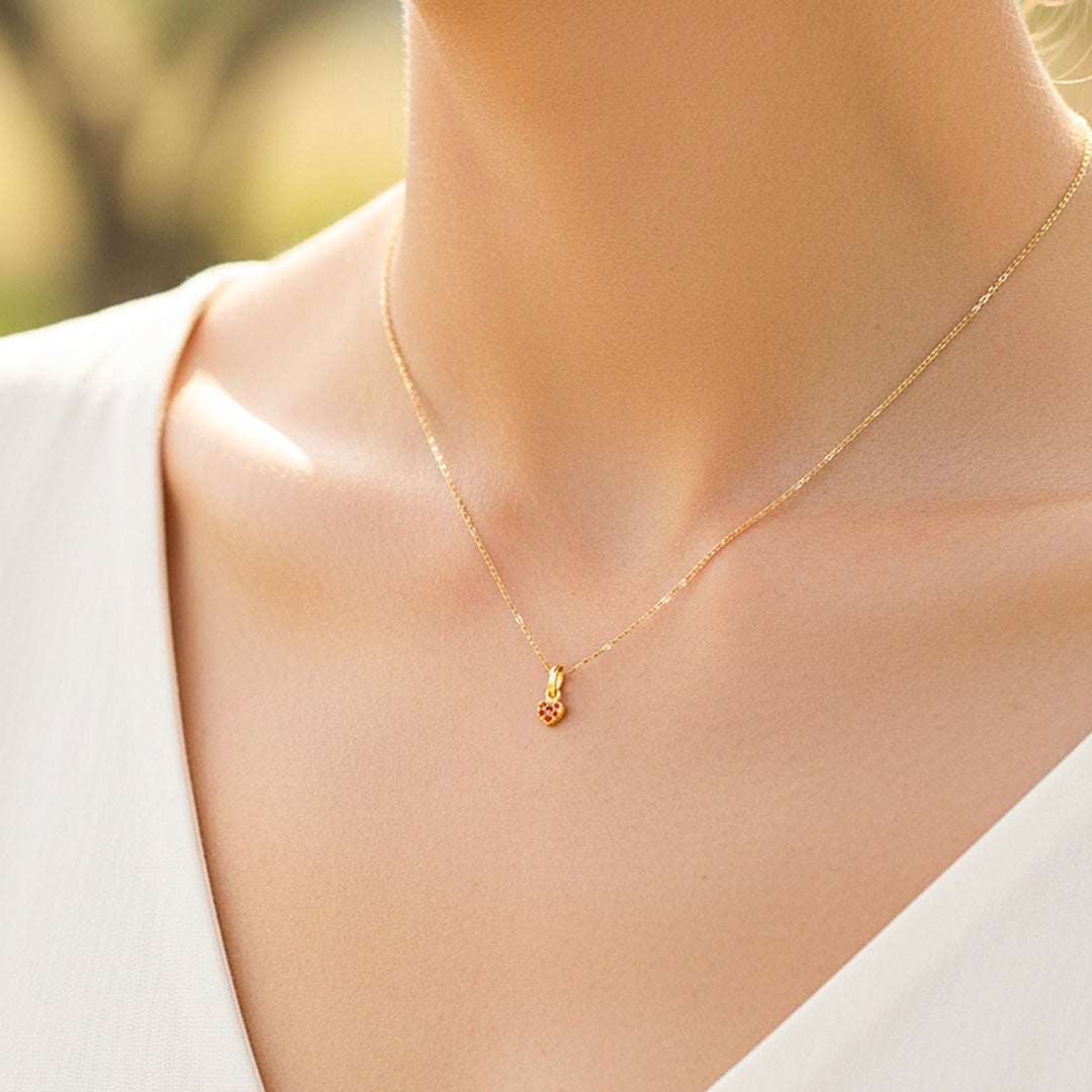 Cuello de modelo usando una cadena con un dije en forma de corazón en oro amarillo de 18 quilates con cristales de color rojo de Joyería Caracas.