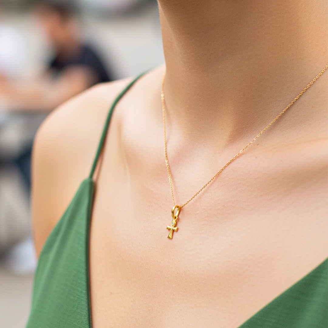 Cuello de modelo usando una cadena con un dije en forma de mini cruz egipcia en oro amarillo de 18 quilates de Joyería Caracas.