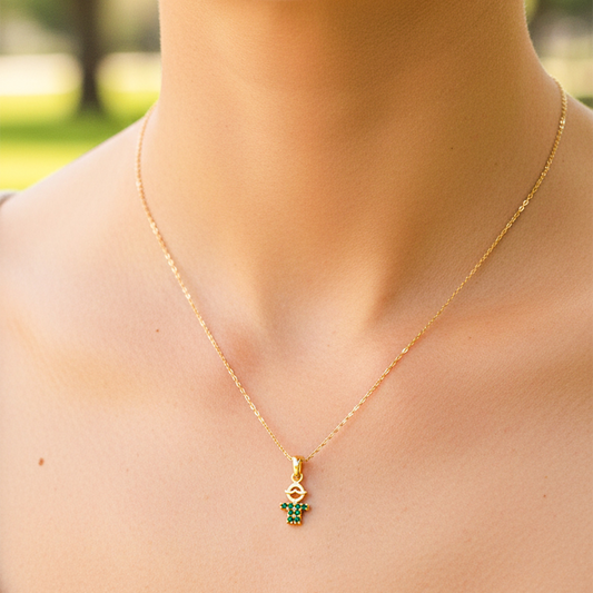Cuello de modelo usando una cadena con un dije en forma de niño en oro amarillo de 18 quilates con cristales verdes de Joyería Caracas.