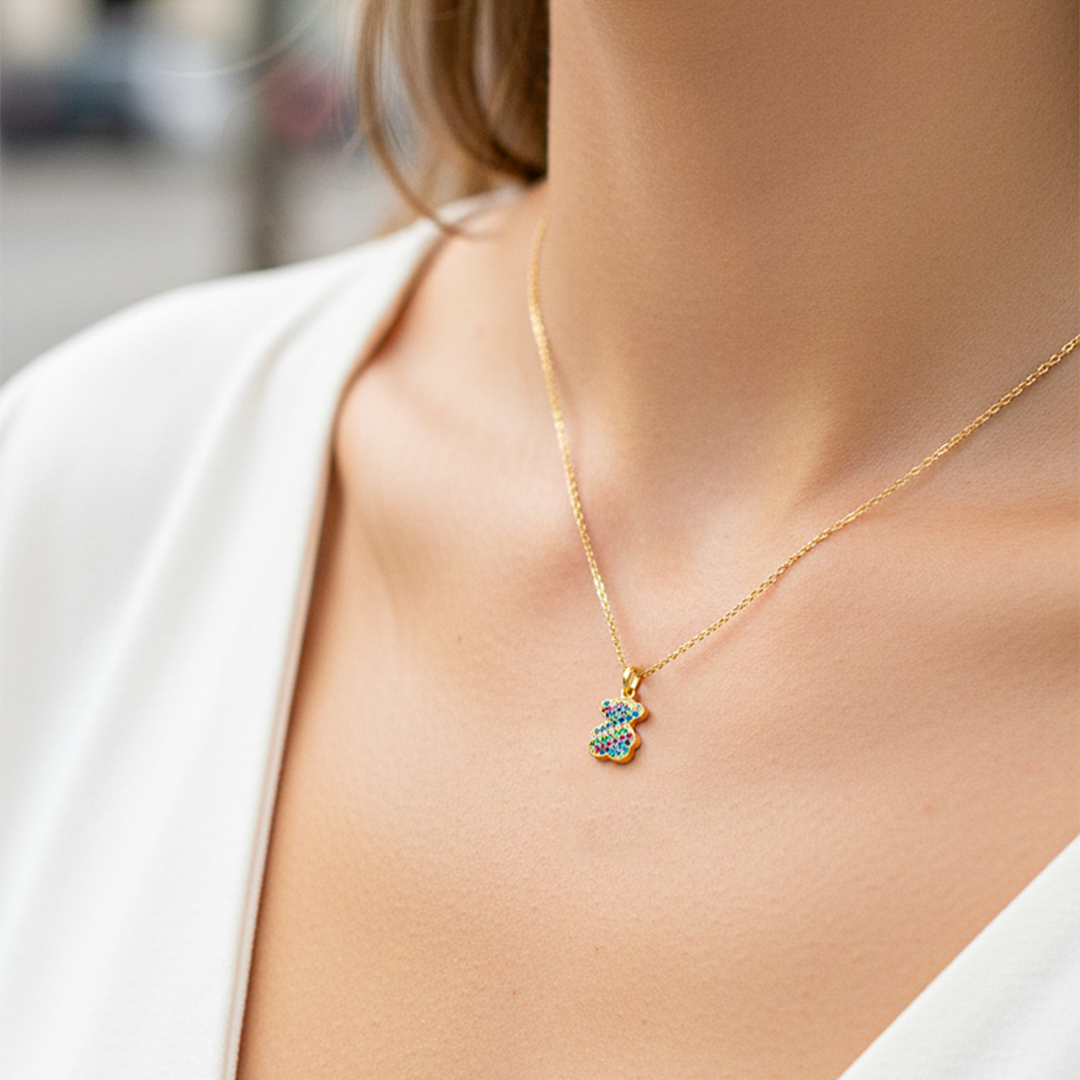 Cuello de modelo usando una cadena con un dije en forma de osito en oro amarillo de 18 quilates con cristales multicolor de Joyería Caracas.