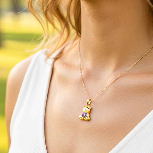 Cuello de modelo usando una cadena con un dije en forma de oso en oro amarillo de 18 quilates con cristales purpuras de Joyería Caracas.