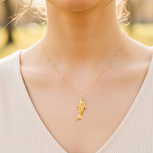 Cuello de modelo usando una cadena con un dije en forma de pescado en oro amarillo de 18 quilates con cristal de Joyería Caracas.