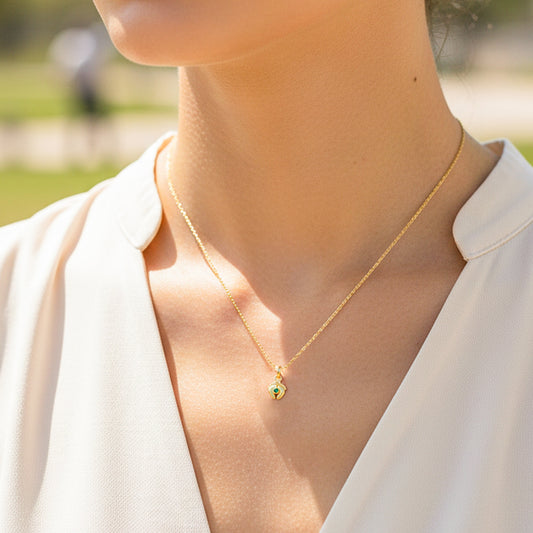 Cuello de modelo usando una cadena con un dije en forma de pies descalzos en oro amarillo de 18 quilates con cristal verde de Joyería Caracas.