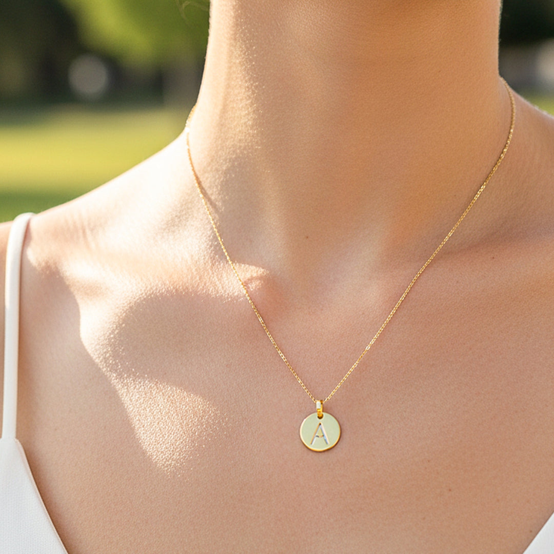 Cuello de modelo usando una cadena con un dije de placa redonda con la letra A en oro amarillo de 18 quilates de Joyería Caracas.