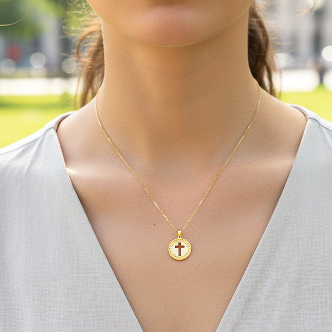 Cuello de modelo usando una cadena con un dije redondo con la silueta de una cruz en oro amarillo de 18 quilates de Joyería Caracas.