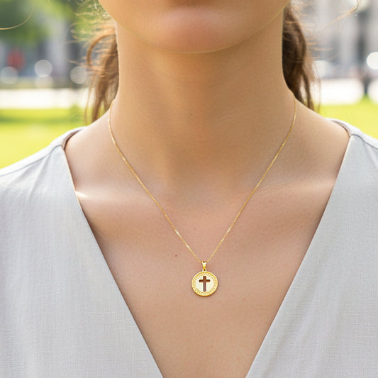 Cuello de modelo usando una cadena con un dije redondo con la silueta de una cruz en oro amarillo de 18 quilates de Joyería Caracas.