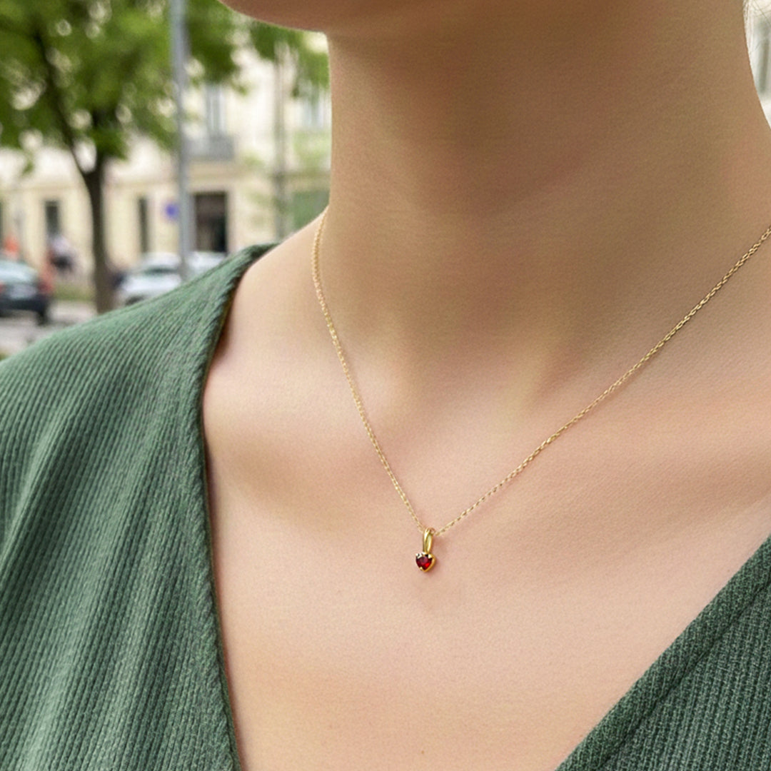Cuello de modelo usando una cadena con un dije en forma de corazón en oro amarillo de 18 quilates con cristal rojo de Joyería Caracas.