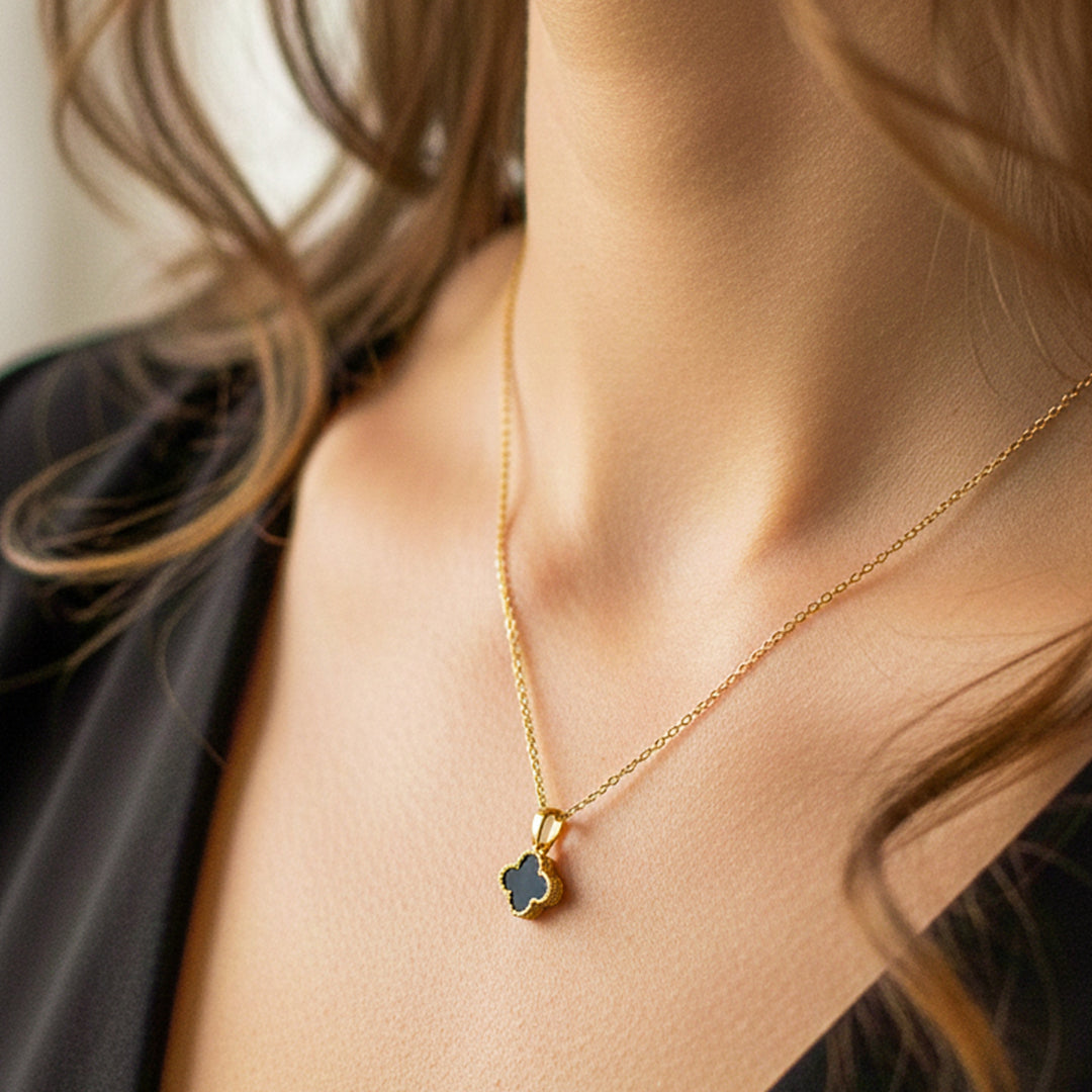 Cuello de modelo usando una cadena con un dije en forma de trébol biselados en oro amarillo de 18 quilates con fondo en negro de Joyería Caracas.