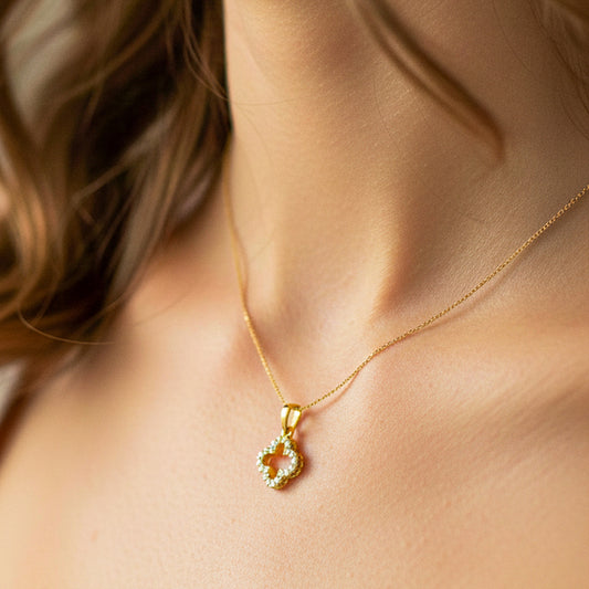 Cuello de modelo usando una cadena con un dije en forma de croquis de trébol en oro amarillo de 18 quilates con cristales blancos de Joyería Caracas.