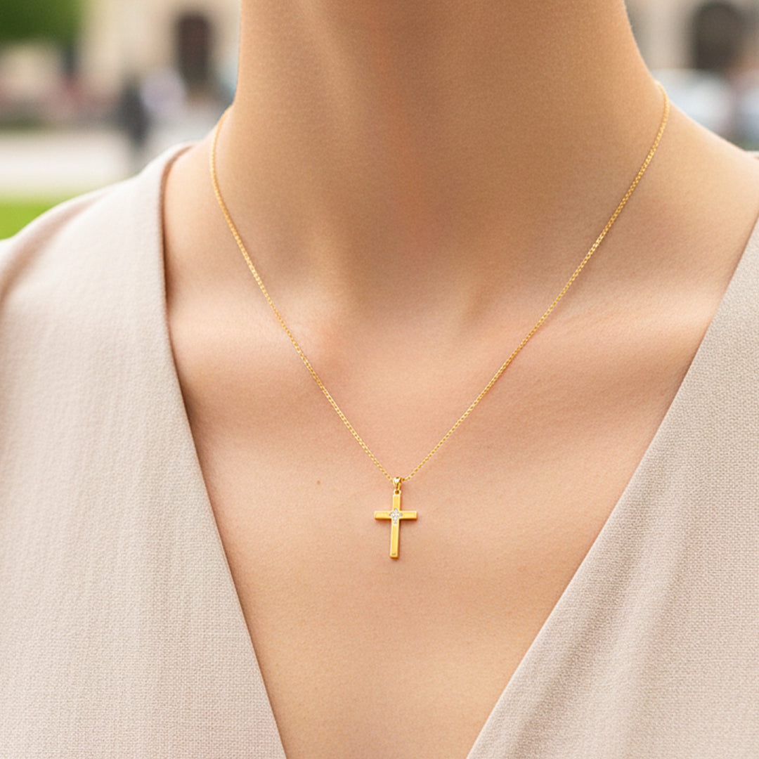 Cuello de modelo usando una cadena con un dije en forma de cruz en oro amarillo de 18 quilates con cristales de Joyería Caracas.