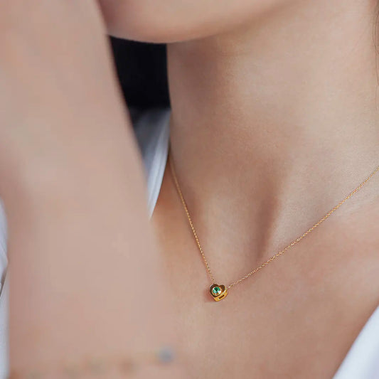 Cuello de mujer con cadena y dije en forma de corazón en oro amarillo de 18 quilates con cristal de color verde, hecho en Joyería Caracas. 