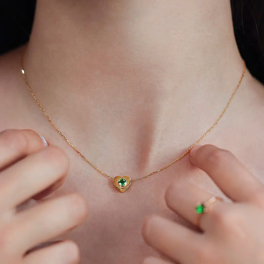 Cuello de mujer con cadena y dije en forma de corazón en oro amarillo de 18 quilates con cristal de color verde, hecho en Joyería Caracas. 