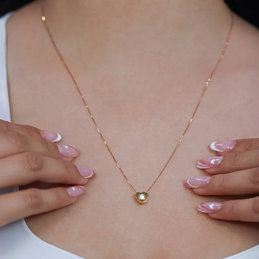 Cuello de mujer con cadena y dije en forma de corazón en oro amarillo de 18 quilates con cristal de color blanco, hecho en Joyería Caracas. 