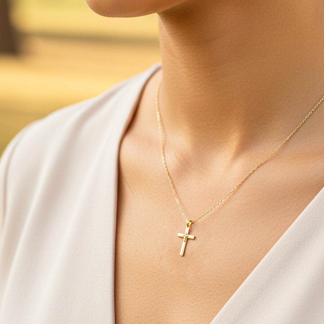 Cuello de modelo usando una cadena con un dije en forma de cruz en oro amarillo de 18 quilates con cristales de Joyería Caracas.