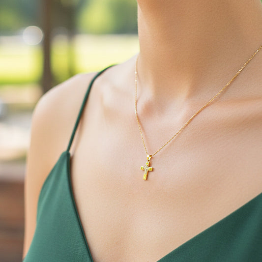 Cuello de modelo usando una cadena con un dije en forma de cruz en oro amarillo de 18 quilates con cristales de Joyería Caracas.