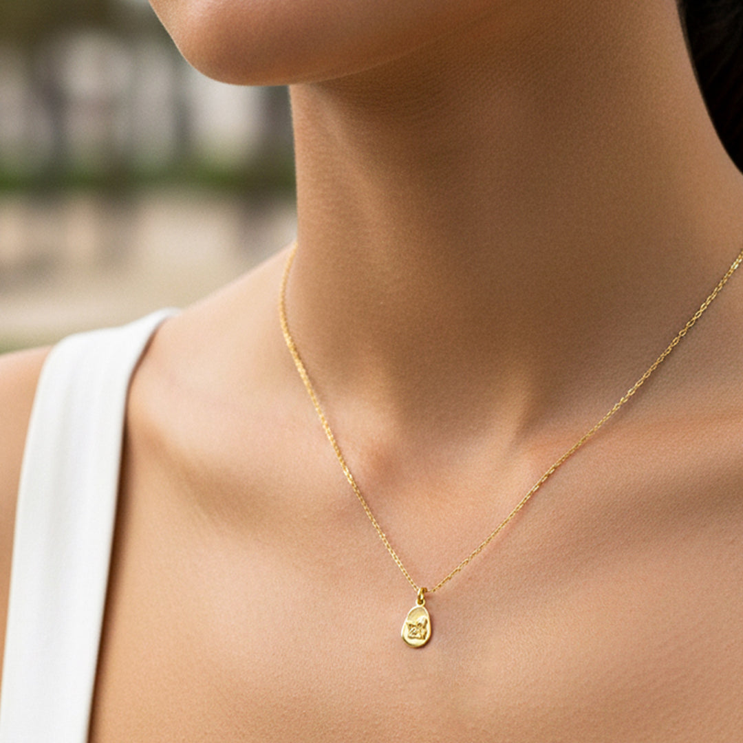 Cuello de modelo usando una cadena con un dije en forma de placa en forma de pera con un angelito en oro amarillo de 18 quilates de Joyería Caracas.