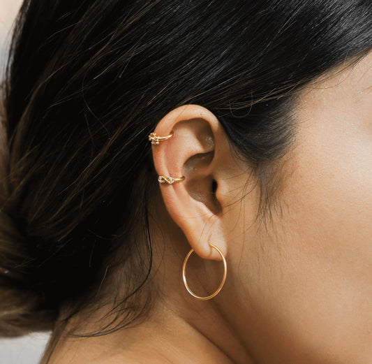 Oreja de mujer con earcuff en forma de infinito en oro amarillo de 18 quilates con cristales de color blanco, hecho en Joyería Caracas. 