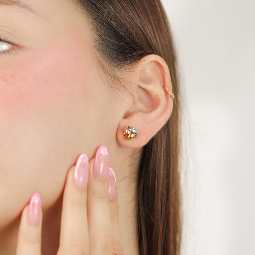 Oreja de mujer con topito en forma de nudo en oro amarillo, blanco y rosa de 18 quilates, hechos en Joyería Caracas. 