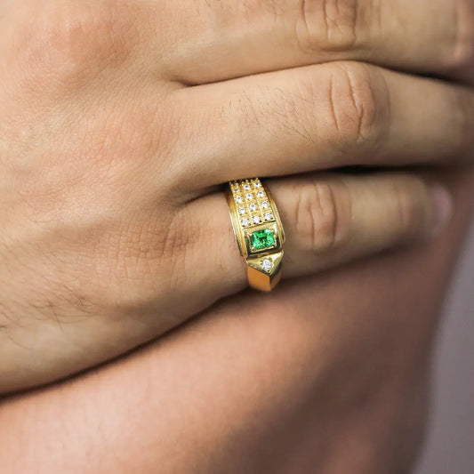 Mano de hombre con anillo en oro amarillo de 18 quilates, con piedra esmeralda de color verde y cristales de color blanco alrededor, hecho en Joyería Caracas. 