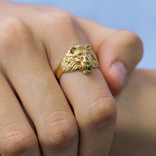 Mano de hombre con anillo en forma de león en oro amarillo de 18 quilates con 2 cristales de color blanco y 1 cristal de color verde, hecho en Joyería Caracas. 