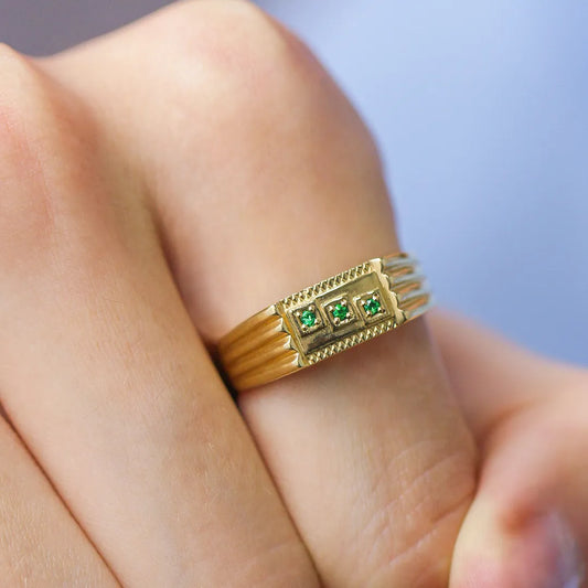 Mano de hombre con anillo en oro amarillo de 18 quilates con 3 piedras esmeraldas de color verde ubicadas diagonalmente en el centro, hecho en Joyería Caracas. 