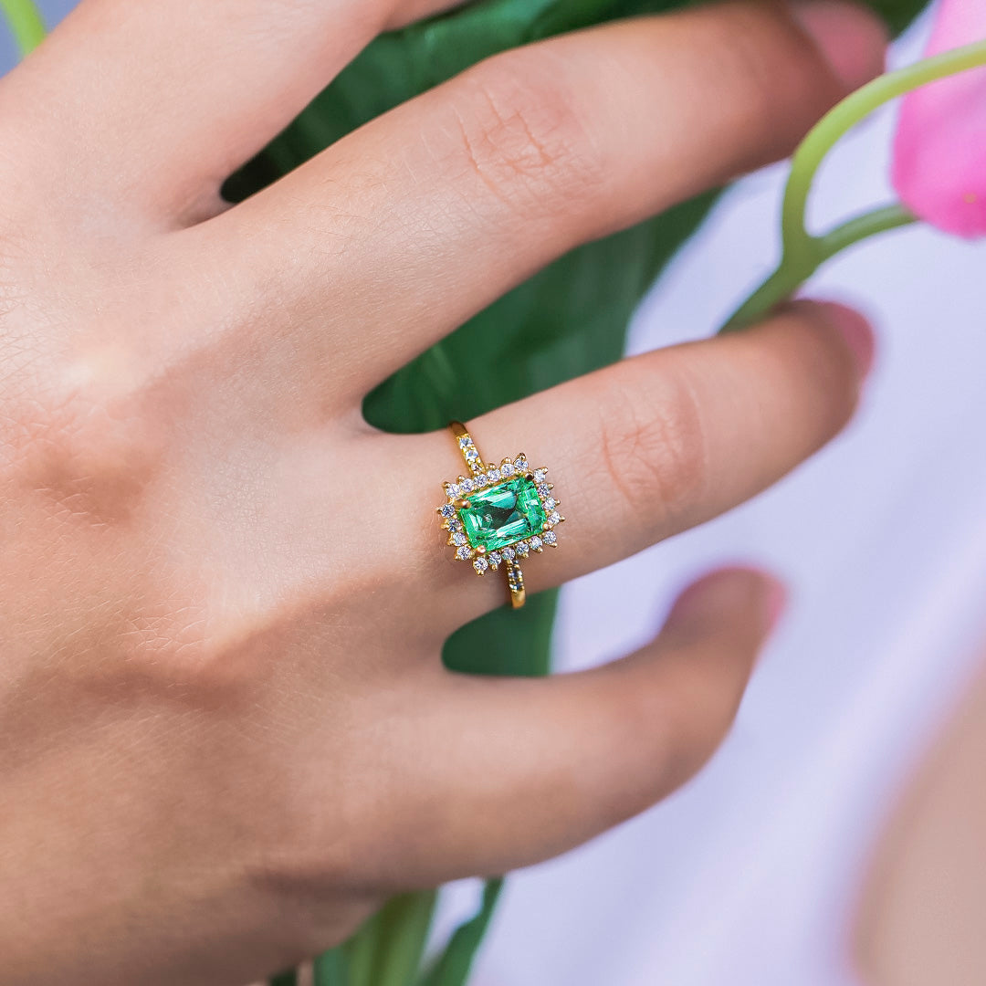 Mano de mujer con anillo en oro amarillo de 18 quilates y esmeralda en color verde con cristales de color blanco, hecho en Joyería Caracas. 