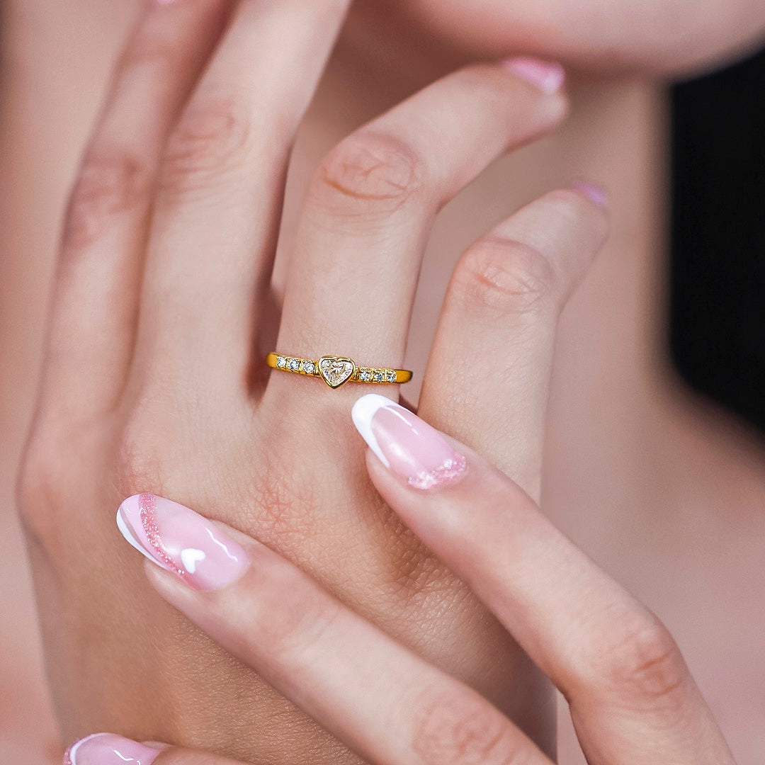 Mano de mujer usando anillo con forma de corazón en el centro de color amarillo de 18 quilates, diamante en forma de corazón de color blanco y 6 diamantes de color blanco alrededor, hecho en Joyería Caracas. 