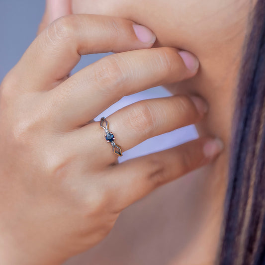 Mano de mujer con anillo en oro blanco de 18 quilates con zafiro de color azul en el centro y 2 cristales de color blanco alrededor, hecho en Joyería Caracas. 