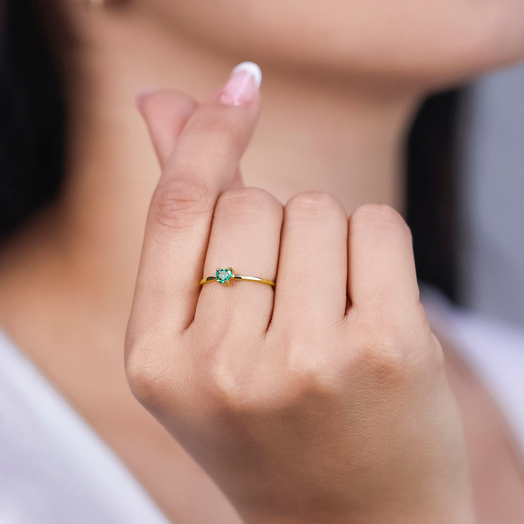 Mano de mujer con anillo en oro amarillo de 18 quilates con piedra esmeralda en forma de corazón de color verde, hecho en Joyería Caracas. 