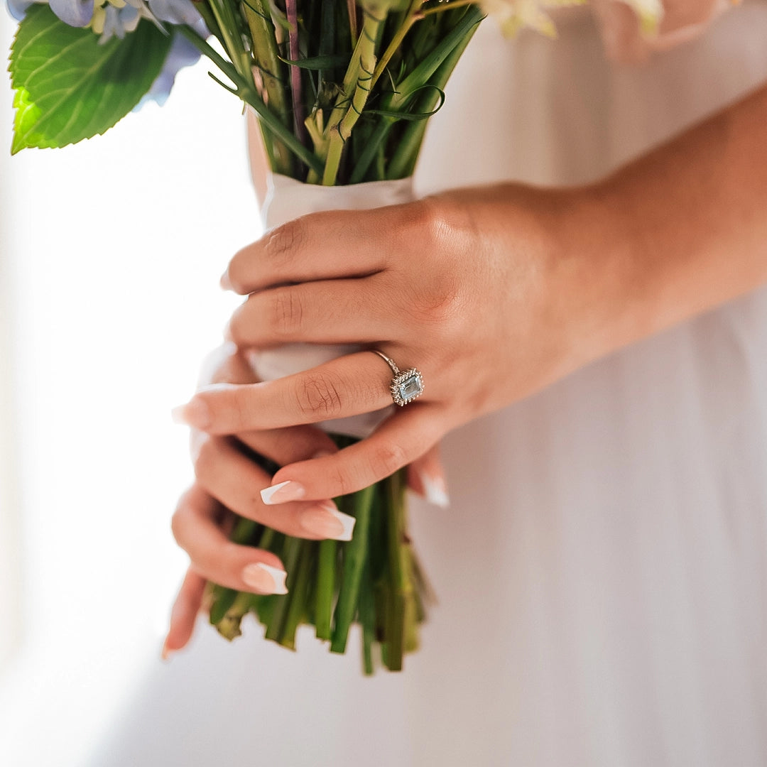 Mano de mujer con un anillo en oro blanco de 18 quilates con una piedra de color celeste de topacio y alrededor de ella diamantes de color blanco, hecho en Joyería Caracas.