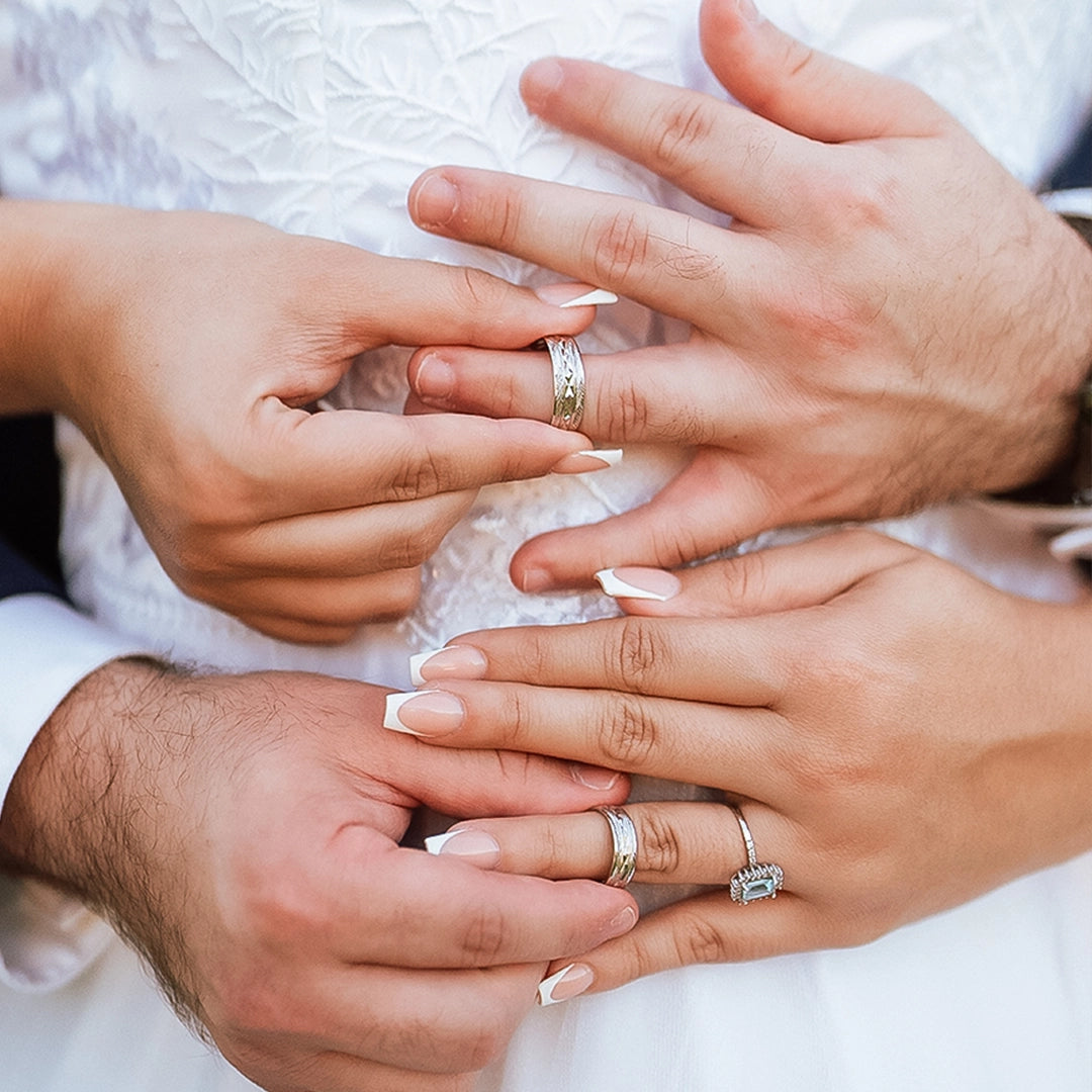 Manos de hombre y mujer en matrimonio sosteniendo cada argolla en oro amarillo de 18k, la cual tiene texturas que lucen cada argolla, hechas en Joyería Caracas. 