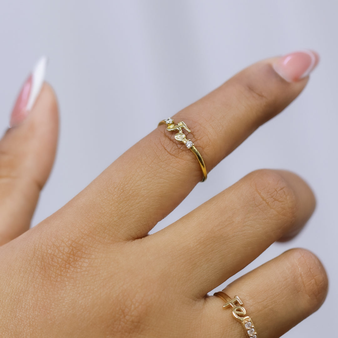 Mano de mujer usando anillo con la palabra Fe en el centro en oro amarillo de 18 quilates con 2 cristales de color blanco, hecho en Joyería Caracas. 