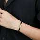 Mano de hombre con pulsera tejida en hilo negro con dije circular con corona en el centro en oro amarillo de 18 quilates con cristales de color blanco, verde y azul, hecho en Joyería Caracas. 