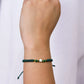Mano de mujer con pulsera tejida en hilo verde, accesorios en color verde y dije de estrella en oro amarillo de 18 quilates, hecho en Joyería Caracas. 