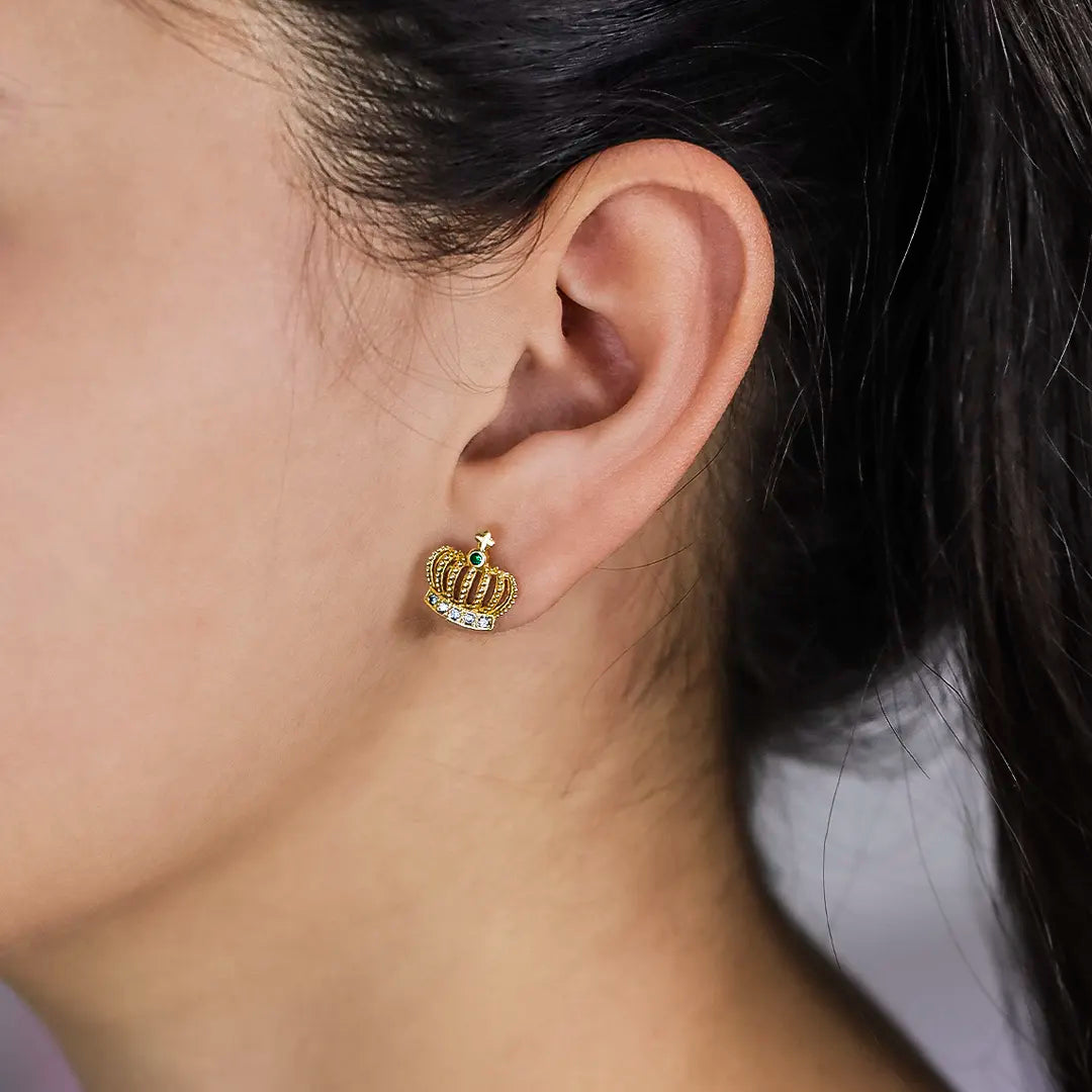 Oreja de mujer con topito en forma de corona en oro amarillo de 18 quilates, un cristal de color verde y 5 cristales de color blanco, hecho en Joyería Caracas. 