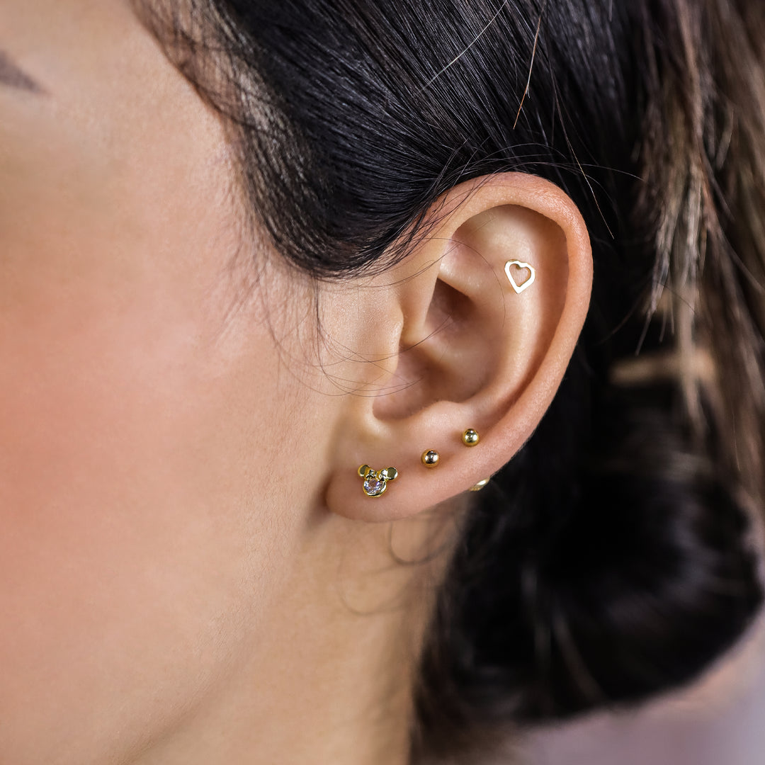 Oreja de mujer con topito en forma de Minnie en oro amarillo de 18 quilates con cristal de color blanco, hechos en Joyería Caracas. 